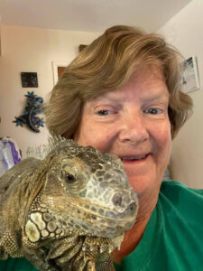 Elaine, wearing a green shirt and smiling at the camera. Calliope is perched on her right shoulder and appears to also be smiling into the camera.