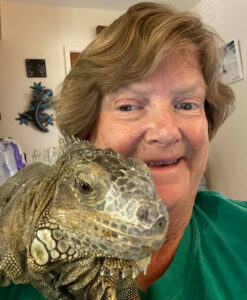 Elaine smiles as a large iguana is perched on her shoulder.