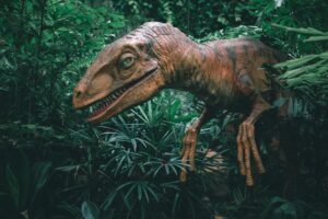 A dinosaur (statue) peeks out from green foliage.