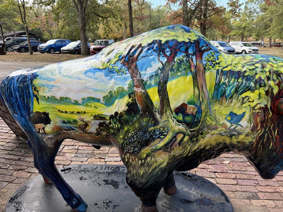 Hand painted bison sculpture with various landscape scenes.