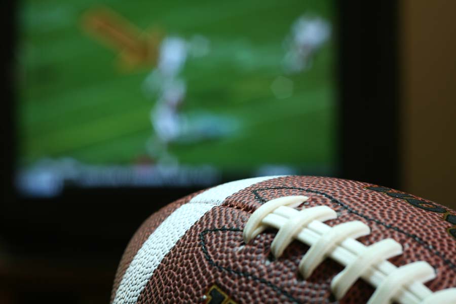 A football with a football game on tv in the background.